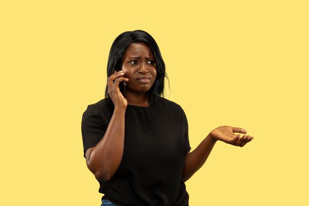 学生年轻的非洲裔美国女性 隔离在黄色的工作室背景下 面部表情美丽的女性半身像人类情感的概念 面部表情通过智能手机交谈漂亮欢呼成功