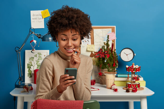 坐着高兴的非裔美国妇女高兴地看着智能手机屏幕 给团友发信息 在网上聊天讨论考试准备反应学生非洲