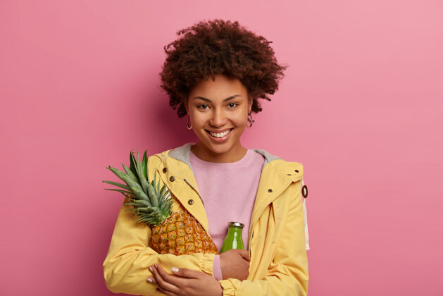瓶子面带微笑的美女拥抱成熟的菠萝和玻璃瓶的绿色冰沙 有正面的表情 健康的营养和维生素高兴女性印象