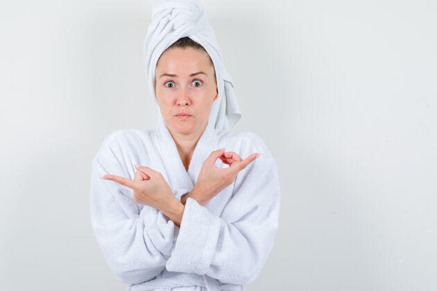 人年轻的女士交叉双臂 指着白色浴衣 毛巾 看上去很内敛前视图女孩浴衣头发