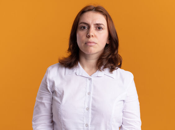 自信身穿白衬衫的年轻女子站在橙色的墙上 神情严肃自信地看着前方年轻严肃表情