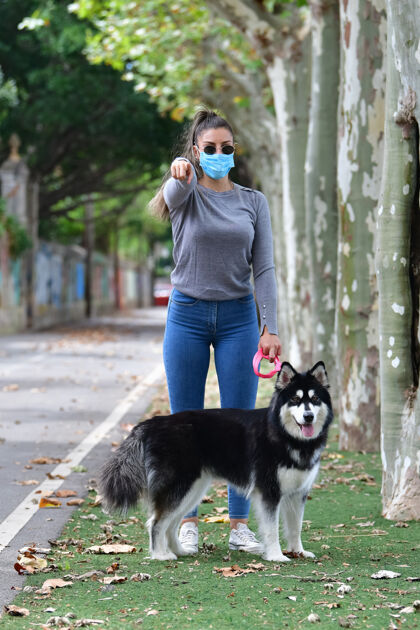 站戴着眼镜和口罩的女人牵着一条狗 指着镜头呼吸环境枫叶