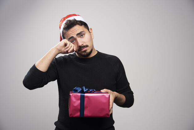 盒子一个年轻人拿着一个礼品盒在灰色的墙上人类圣诞老人礼物