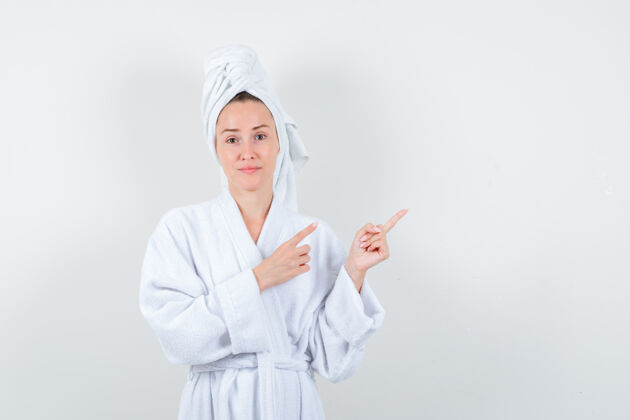 时尚年轻女子指着右上角的白色浴衣 毛巾 看上去很懂事 前视图显示卷发魅力