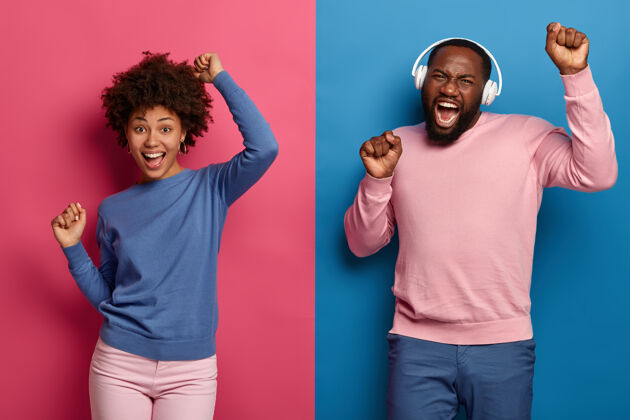 活跃富有魅力的快乐的黑人男女在音乐的节奏中举手跳舞 戴上耳机 对着蓝色和粉色的空间摆姿势美国舞蹈音乐
