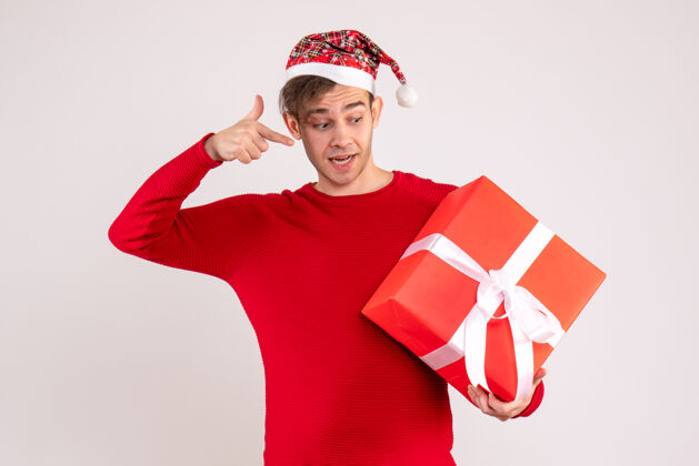 微笑前视图：戴圣诞帽的年轻人指着白色背景上的礼物背景指着圣诞节