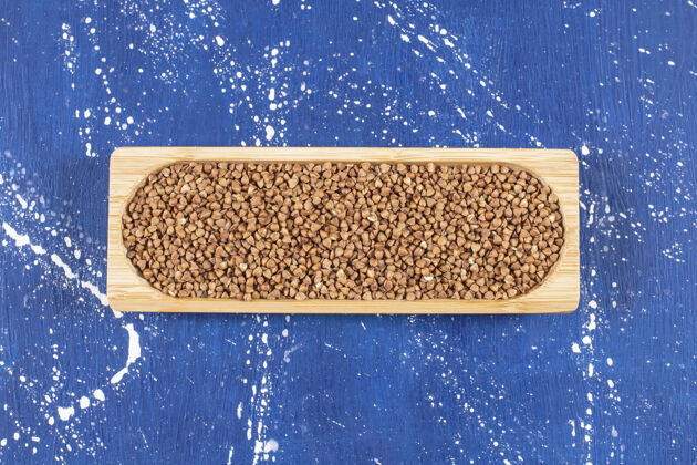 素食主义者蓝色表面上木托盘上一堆荞麦的俯视图配料烤素食者