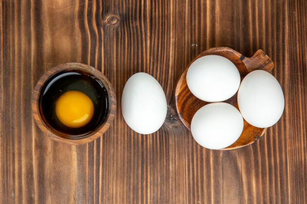 早餐俯视整个生鸡蛋在棕色的木头表面用餐早餐木头鸡蛋景观生的鸡肉