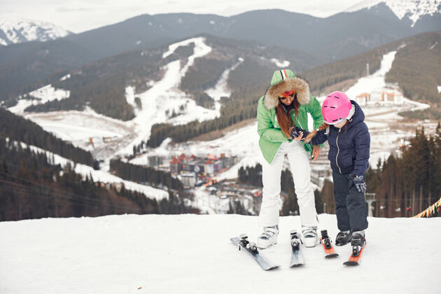 年轻妈妈带着女儿在滑雪雪山上的人们护目镜人眼镜
