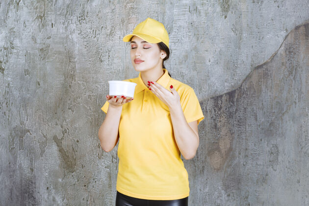 成人穿着黄色制服的女快递员手里拿着一个外卖杯 闻着产品的味道味道职员年轻人
