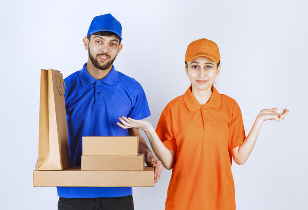 休闲穿着蓝黄制服的男女快递员手里拿着纸板外卖盒和购物包工人成人姿势