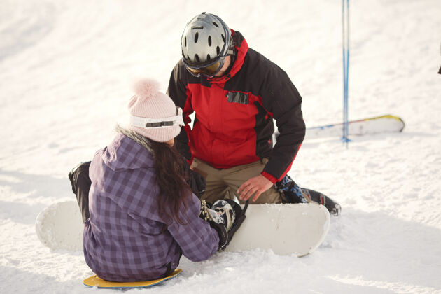 山女孩试图爬上滑雪板男孩给了女孩一只手紫色套装运动下雪滑雪