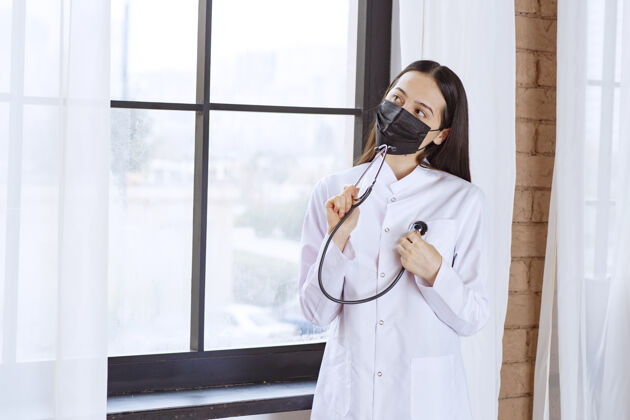 健康戴着黑色口罩的医生站在窗边用听诊器检查心跳诊所模特医学