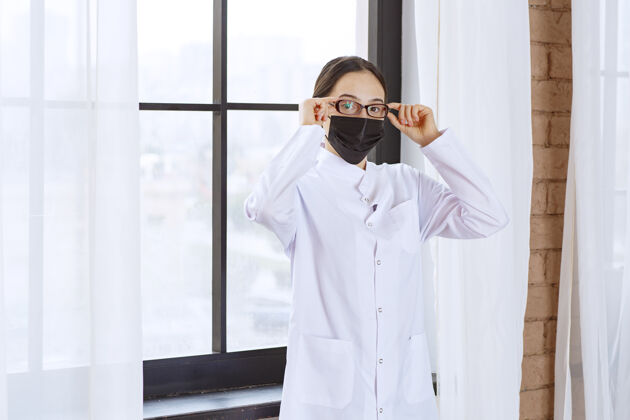 装备戴着黑面具和眼镜的医生站在窗边健康妇女预防
