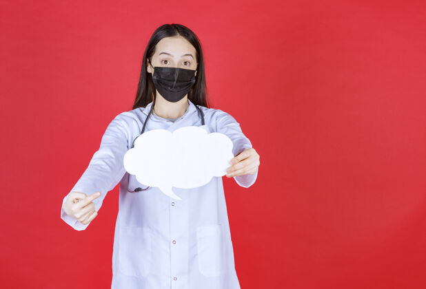 妇女女医生带着听诊器 戴着黑色面罩 手里拿着一张云状的空白问讯台细菌姿势医院