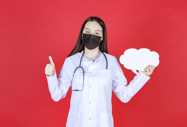 医院女医生戴着听诊器 戴着黑色口罩 手持一张云状的空白问讯台 展示着享受的标志护理姿势项目