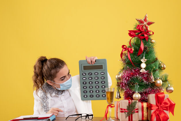 工作前视图戴面具的女医生手持计算器桌子设备圣诞节