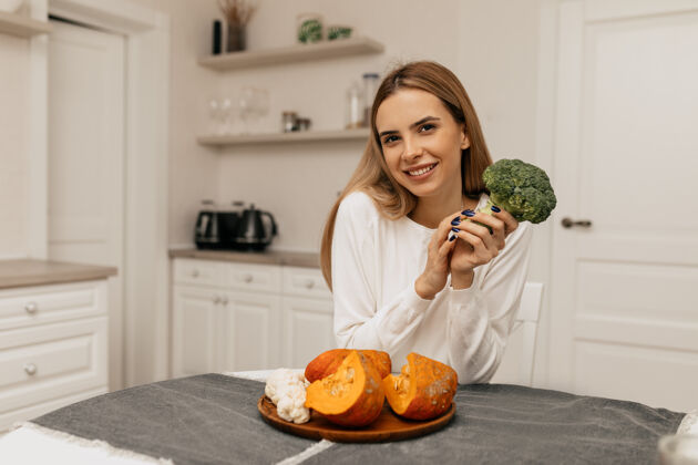 积极美丽的微笑女士坐在厨房里 手里拿着花椰菜和南瓜准备做饭金发拥抱平衡