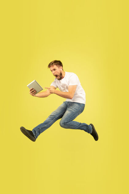 男性黄色背景上的快乐跳跃人的全长肖像平板电脑休闲男孩
