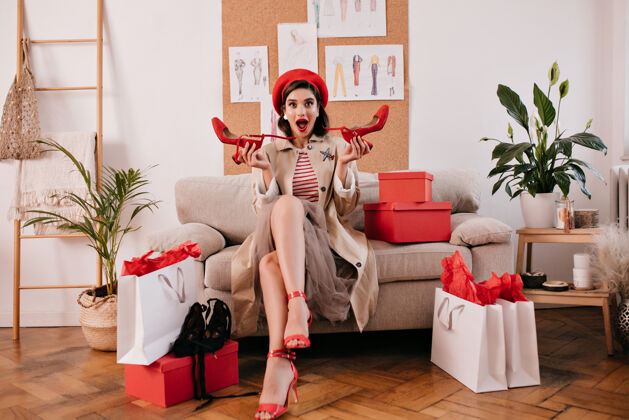 优雅购物后的女人穿着新衣服坐在沙发上漂亮时髦的女孩拿着红色的现代鞋坐在沙发上女士贝雷帽姿势