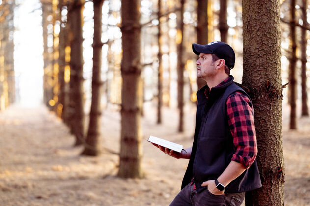 树干一个男人拿着一本书在森林里摆姿势的选择性聚焦镜头阅读人教育
