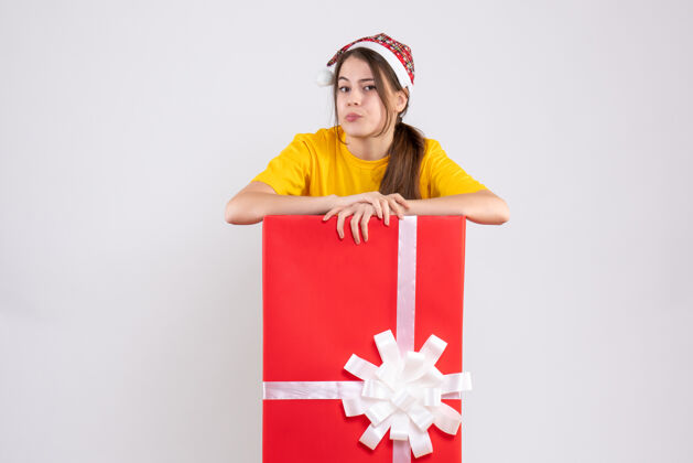 快乐大圣诞礼物后面站着一个戴圣诞帽的女孩人漂亮包