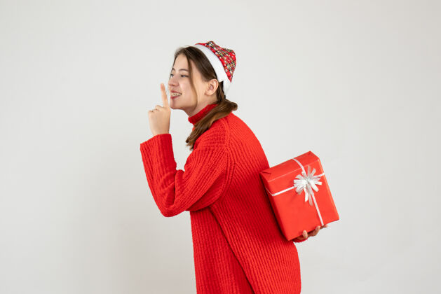 空间前视图兴奋的女孩与圣诞帽藏在背后她的圣诞礼物 使嘘标志背部圣诞节人