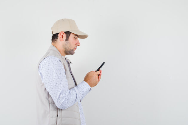 帅哥年轻人手里拿着手机 穿着米色夹克 戴着帽子 表情严肃正面图前面电话男人