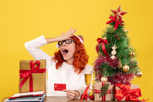 微笑前视图女医生拿着银行卡在圣诞礼物和圣诞树周围情绪成人银行