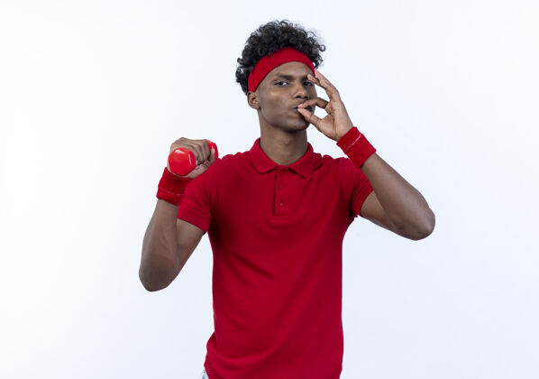 哑铃自信的年轻美国黑人运动型男子 戴着海带和腕带 肩上抱着哑铃 在白色背景上展示着独特的美味手势运动肩膀握着