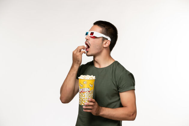 视图正面图身着绿色t恤的年轻男性手持爆米花包戴着d墨镜在白墙上拍摄电影孤独电影院男性电影电影成人电影