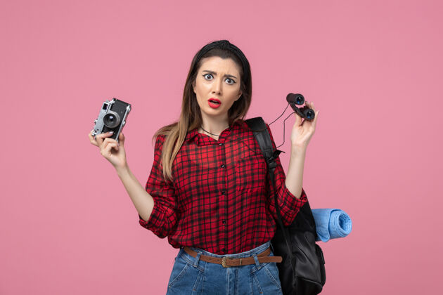 脸前视图年轻女性用望远镜和相机对粉红色背景色的女人人类漂亮望远镜电话