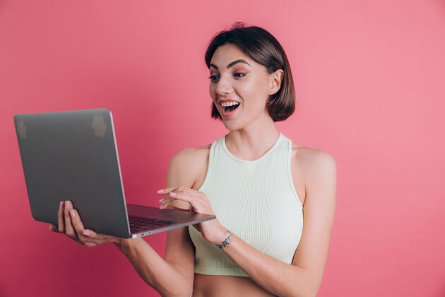 工作粉色背景的女人张着嘴拿着笔记本电脑使用欢呼成人