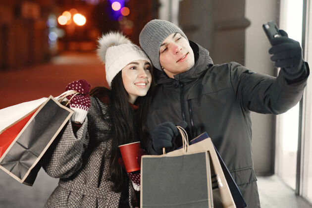 雪带着购物袋的年轻夫妇的户外夜照购物年轻十二月