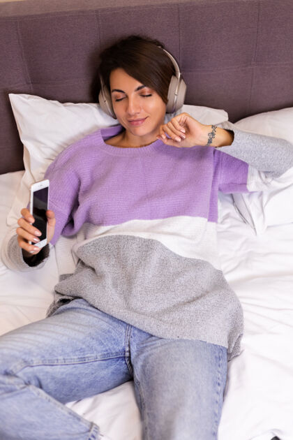 科技快乐的女人在家舒适的床上穿着暖和的衣服套头衫 听音乐舒适冷静枕头