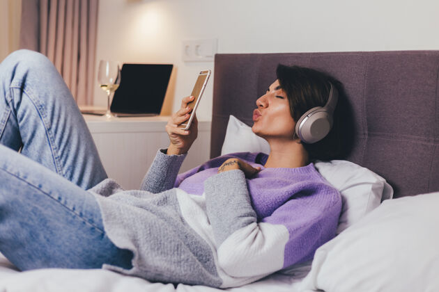 睡觉时间快乐的女人在家舒适的床上穿着暖和的衣服套头衫 听音乐瞌睡年轻女人床