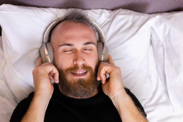 科技快乐的白人男子戴着耳机躺在床上听他最喜欢的音乐 独自休息 跳舞休息家伙享受