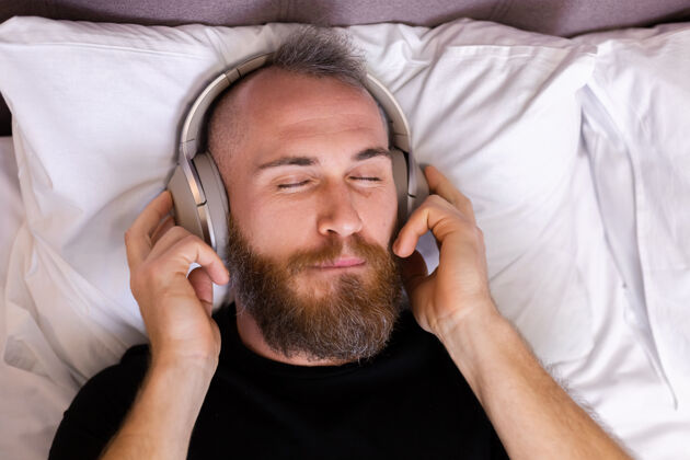 休息快乐的白人男子戴着耳机躺在床上听他最喜欢的音乐 独自休息 跳舞移动耳机舒适
