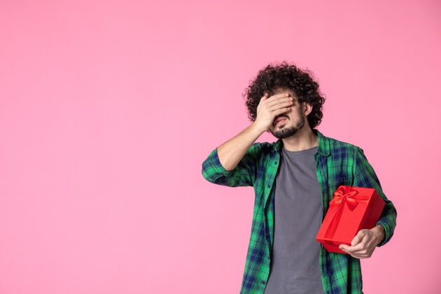 年轻人浅粉色墙上红色包裹的年轻男性正面图包装礼物休闲