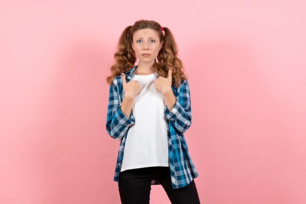 漂亮正面图：穿着格子衬衫的年轻女性在粉色背景上摆姿势模特儿情感童男少女肖像姿势衬衫