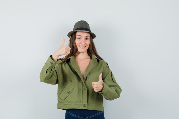 夹克穿着夹克裤子帽子的年轻女士向上竖起大拇指 看起来很高兴时尚欢快拇指