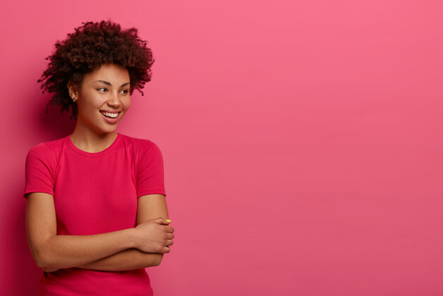 一旁《快乐的千禧一代女孩》的一个单独的镜头看起来很开心 穿着休闲服 注意到一些有趣的事情 站在粉色的墙上 空白的地方放着你的广告内容或文字女人享受室内