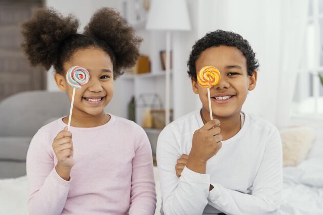 在一起两个微笑的兄弟姐妹与棒棒糖摆姿势的前视图棒棒糖水平娱乐