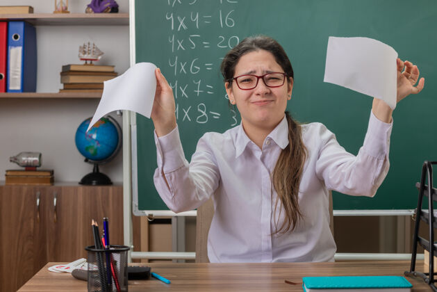 桌子这位戴眼镜的年轻女教师坐在教室的黑板前 一副不高兴的样子 撕扯着一张纸学校坐着教室