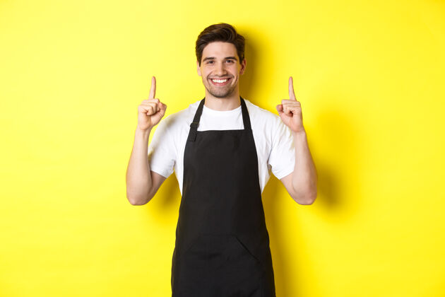 男人帅气的咖啡师展示广告 咖啡店促销 手指向上 站在黄色背景下年轻成人时尚