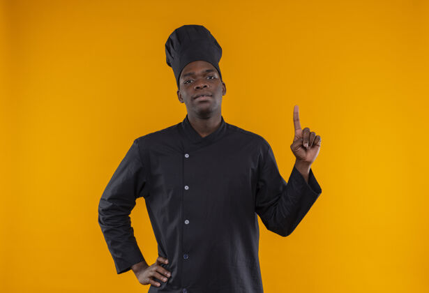 复制身着厨师制服的年轻自信的美国黑人厨师站起身来 把手放在腰上 放在橘子上 留有复印空间信心点制服