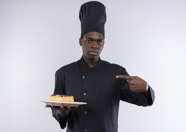 烹饪身着厨师制服的年轻美籍黑人厨师手拿蛋糕 指着白色盘子上的蛋糕 上面留有复印空间制服持有复制