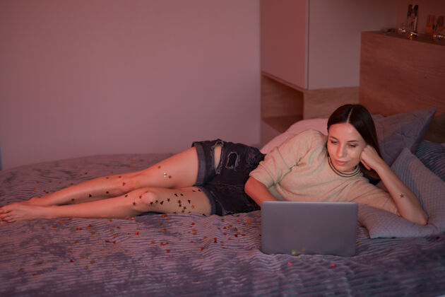 房子美丽的女人和她的家人和朋友在网上庆祝使用笔记本电脑 喝咖啡与五彩纸屑在床上电脑会议通讯