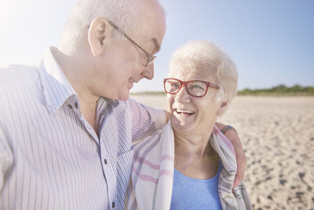 享受老年夫妇在沙滩 退休和暑假的概念拥抱毯子休息