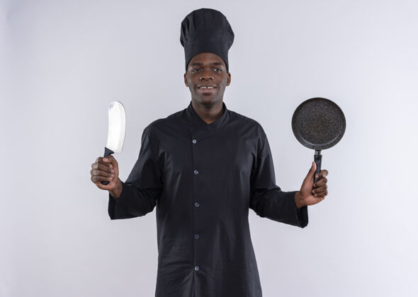 制服身着厨师制服的年轻美籍黑人厨师手持小刀和煎锅 看着白色的一面 留着复印空间壁板厨师副本